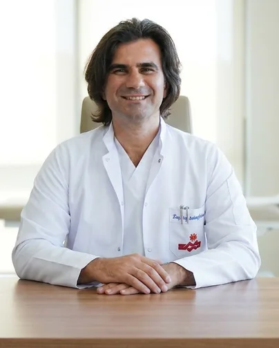 Prof. Dr. Çağatay Çağlar in his consulting room, seated at his desk in a white coat.